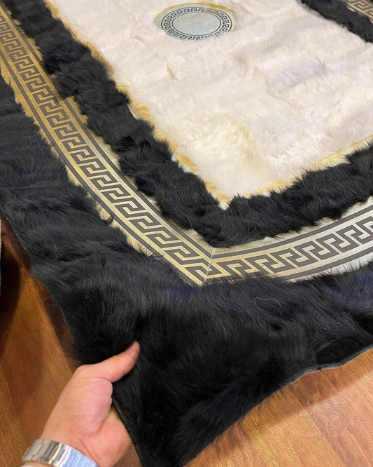 Close-up of a handmade natural sheepskin rug in black and white with a decorative border being held by a hand