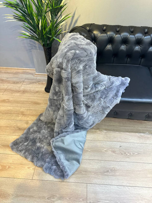 Gray natural fur blanket made from Rex rabbit fur draped on black leather sofa in modern living room