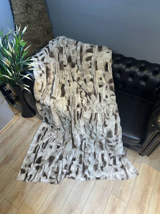 Handmade real rabbit fur blanket throw draped on black leather sofa with wooden floor and green plant nearby