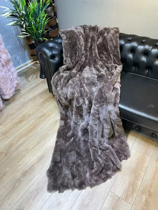 Luxury natural leather rabbit fur throw blanket draped on black leather sofa in cozy living room setting