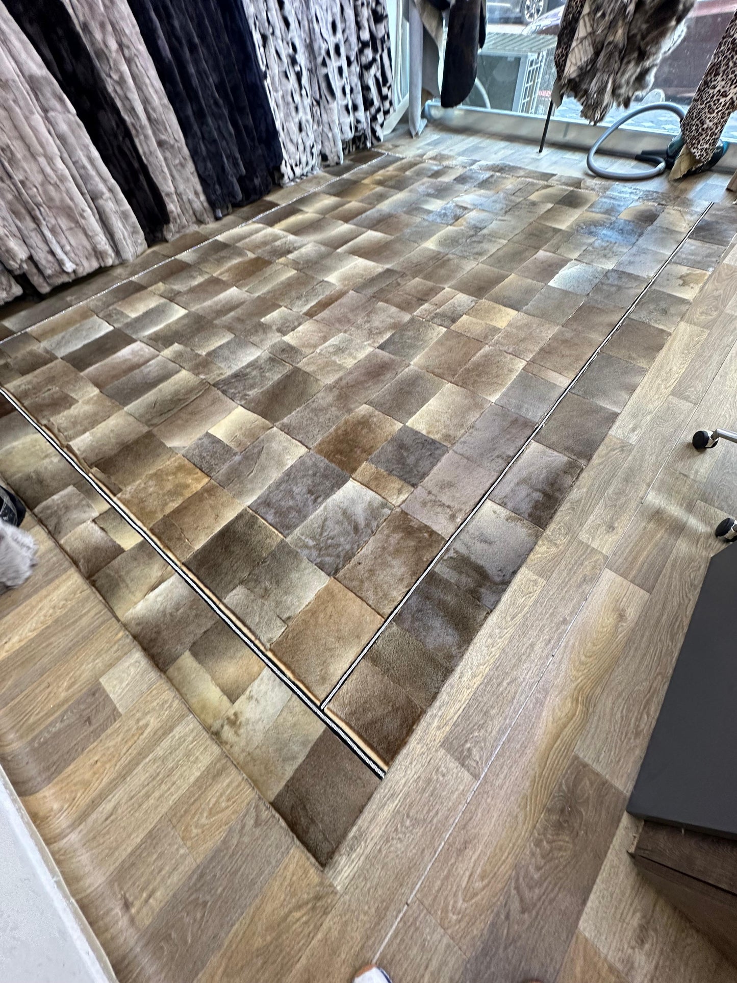 Handmade brown patchwork cowhide rug with beige accents on wooden floor in showroom