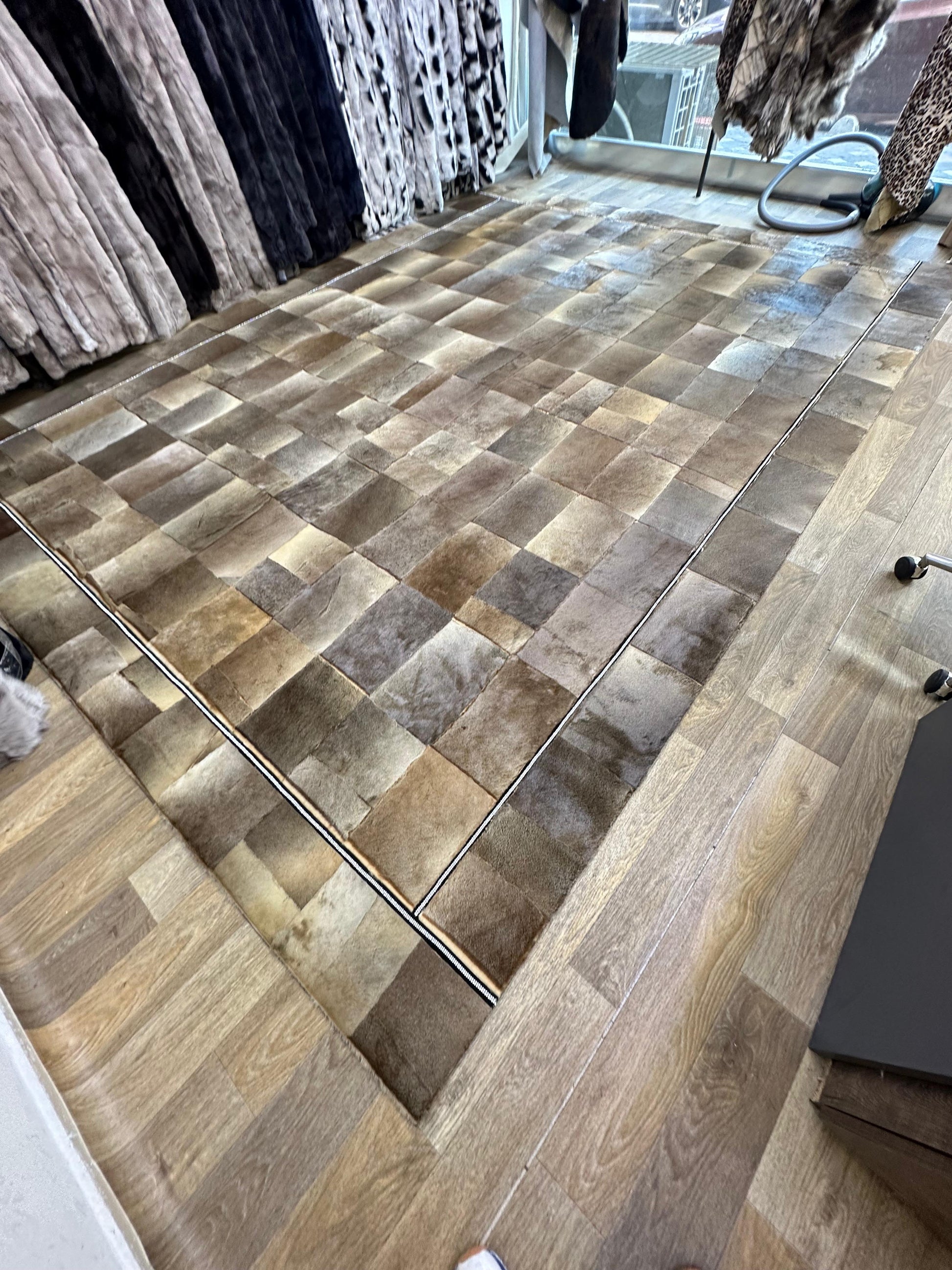 Handmade brown patchwork cowhide rug with beige accents on wooden floor in showroom