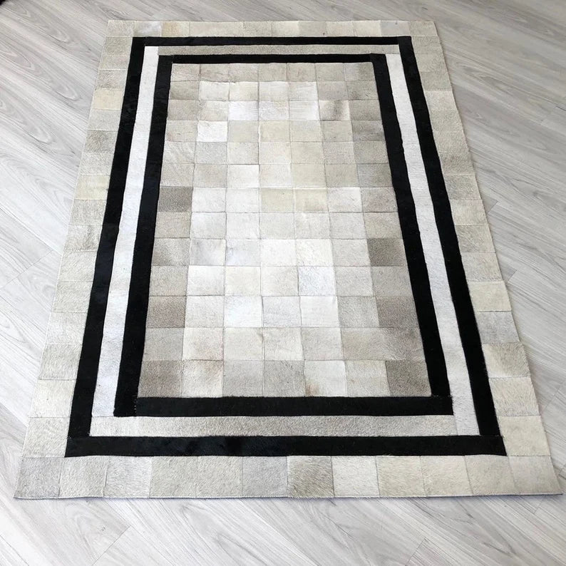 Handmade white cowhide patchwork rug with black borders on wooden floor